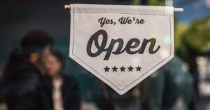 Sign in a window that states, “Yes, We’re Open” with customers blurred in the background.